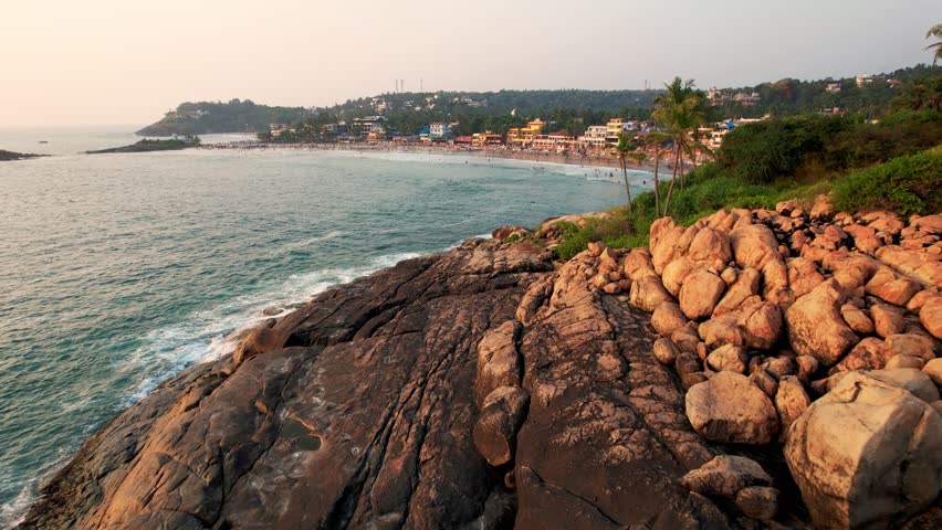 Aerial View of the Turquoise Waves Crash Against Rocky Coastline, sea weaving around boulder-strewn coastlines. Kovalam beach, India, Kerala. 