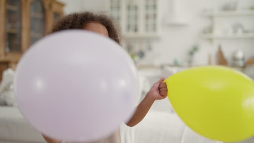 Happy little sister and brother playing together at home, fighting by balloon. Joyful children have fun, active pastime in birthday party, African American kids with balloons smiling and laughing