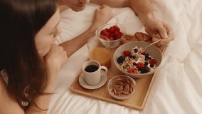 Romantic moment as boyfriend feeds girlfriend breakfast in bed, featuring muesli with yogurt, fresh coffee, and a cozy atmosphere. - Powered by Shutterstock - Get 15% off with code: PIKWIZARD15