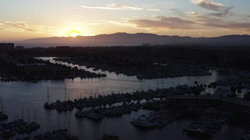 An aerial parallax shot of docked sailboats silhouetted against the sunset in Los Angeles, California