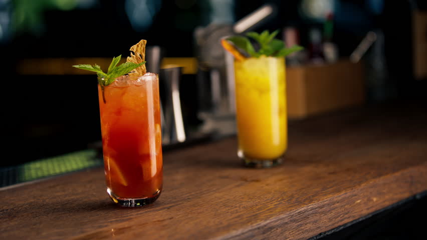 close-up on dark background two tall glass with a yellow-orange cocktail decorated with mint and dried orange