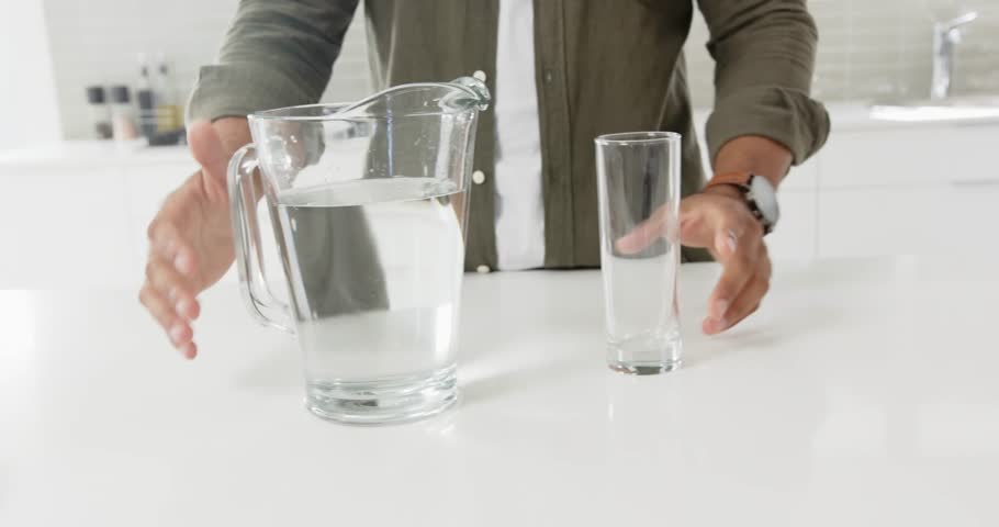 Lifestyle videos indoor of people doing activities at home, holding glass of water, man standing in bright modern home setting.  pouring a liquid into a cup, pouring water in a cup and drinking it