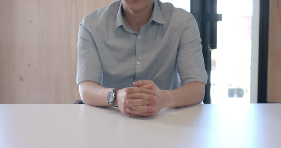 Close up of people talking to the camera, businessman sitting at desk with hands clasped, wearing watch and shirt. only body is visible, sitting,  talking to the camera with exaggerated hand movements
