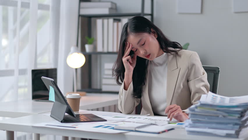 Businesswoman struggling with paperwork while experiencing a headache, showcasing the stress and pressure of office work