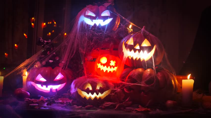 Creepy scary Halloween decorations Jack-o-lanterns carved pumpkins flickering lights among the thick fog covered with cobwebs, party background.