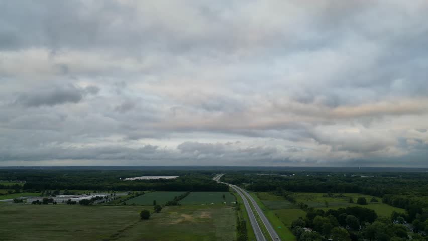 A broad aerial view showcasing a rural highway stretching through vast fields under an overcast sky.