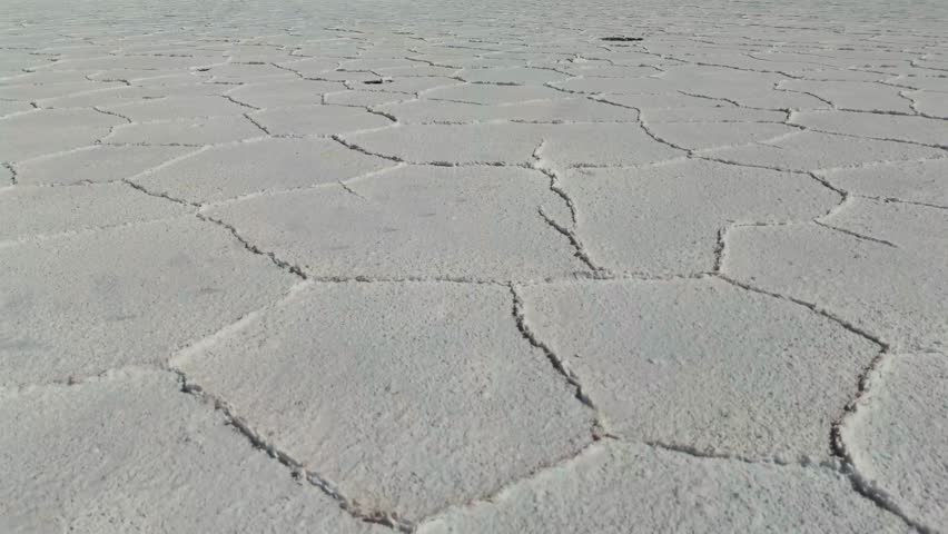 Drone aerial views nature scenes, a desert setting, a vast white salt flat with hexagonal patterns cracked across its surface, pan forward
