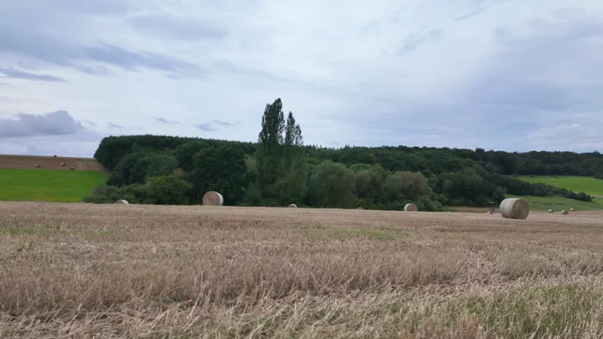 Time-Lapse Photography, sky, a half-dried grass field with a few hay bales around, green areas, and trees in the background under a cloudy sky

