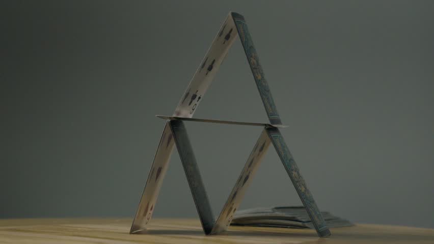 Photography for dynamic scenes, collapse, a hand throws a playing card at a card house, causing the structure to collapse.