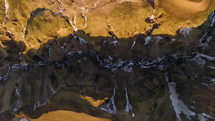 Aerial top down sunrise in deep Icelandic canyon with ice river and mossy cliffs
