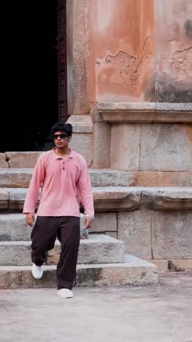 An Indian man in a kurta and goggles walks through a monument, blending traditional attire with modern style against historic architecture.