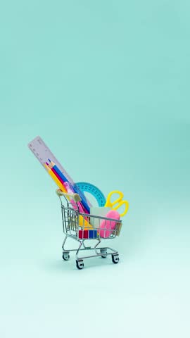 Shopping trolley with stationery items and school supplies moving on blue background. back to school and education background concept. Shopping cart, supermarket trolley. Stop motion animation vertica