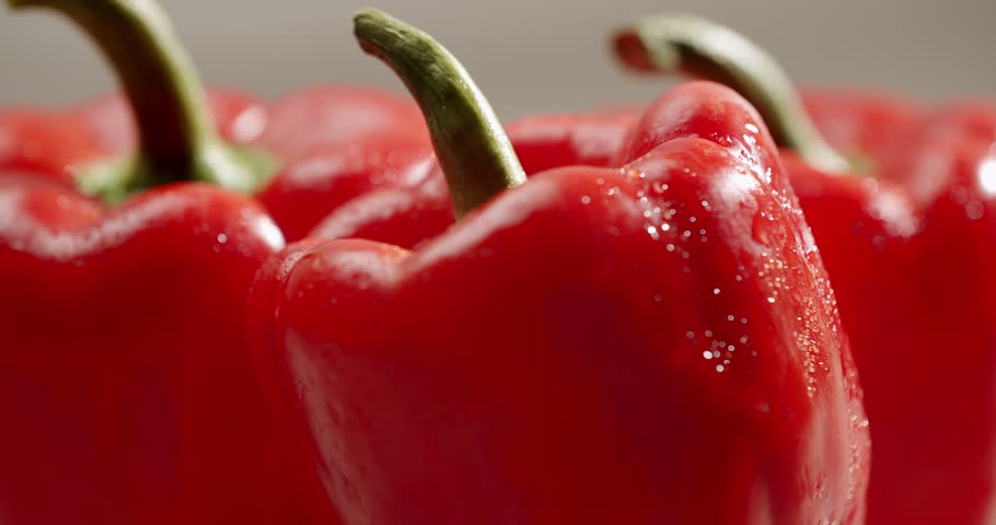 A vibrant close-up image of fresh red bell peppers with stems, placed on a light surface, conveying freshness and natural goodness. Close-Up Shot Of Fresh Red Bell Peppers On A Light Surface