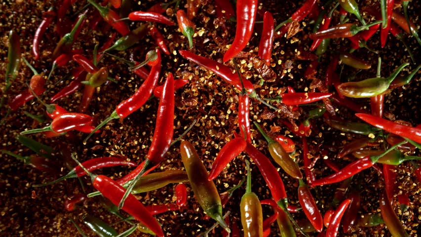 Super slow motion of flying and rotating red chilli peppers. Filmed on high speed cinema camera, 1000 fps, placed on high speed cine bot, following the target. Black background. Speed ramp effect.