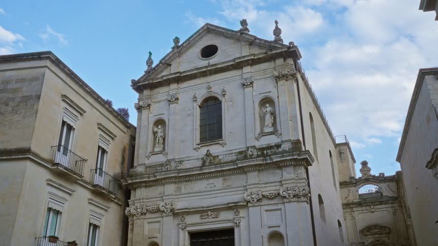 Historic baroque church facade in lecce, puglia, italy with detailed statues, columns, and architectural elements under a partly cloudy sky.