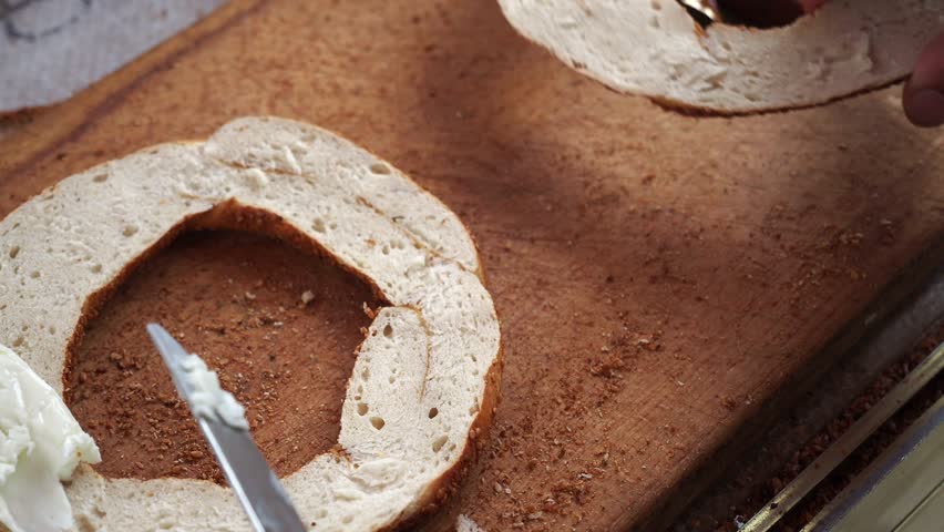 The delightful act of spreading creamy cream cheese generously on a fresh, warm bagel