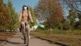 A woman wearing a protective mask is riding a bicycle in an autumn park, with trees with yellow leaves lining the path - Powered by Shutterstock - Get 15% off with code: PIKWIZARD15