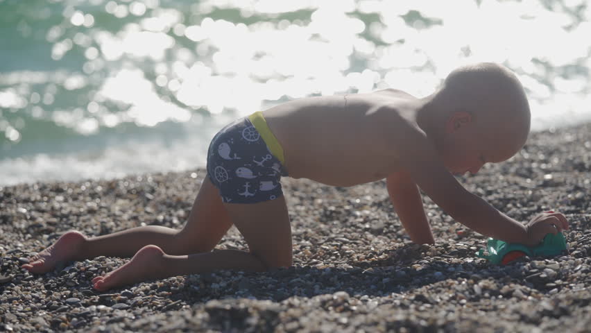 Little boy playing on the beach in summer. Child with shaved head by the sea. Children summer vacation. Yevpatoriya, Crimea