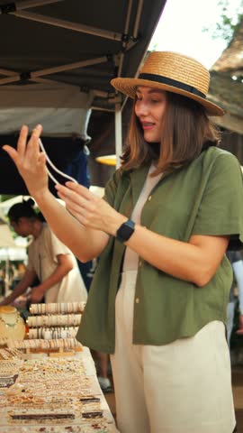 Young Woman Picks Out Handmade Jewelry at the Weekend Jing Jai Market, Having Fun. Vacation, Asian Culture, Shopping Concept, Vertical Screen