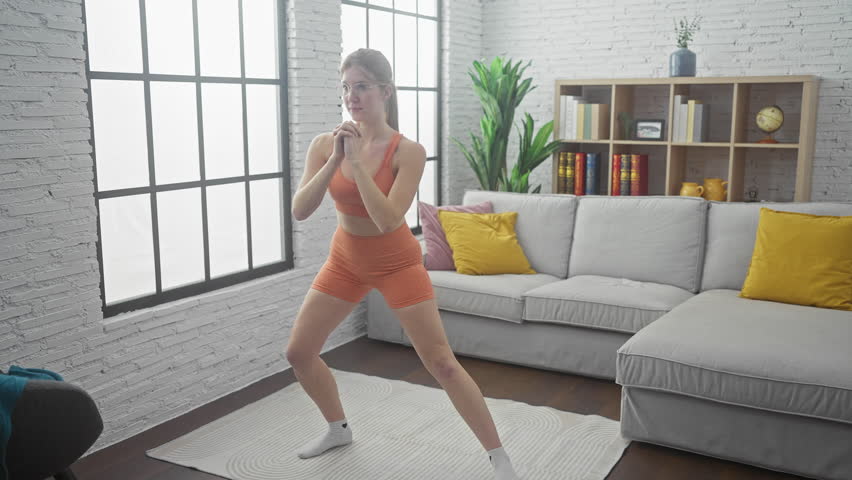 A young woman in activewear performs a squat exercise in a modern apartment