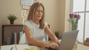 Mature woman adjusting glasses while working on laptop in a cozy home office setting - Powered by Shutterstock - Get 15% off with code: PIKWIZARD15