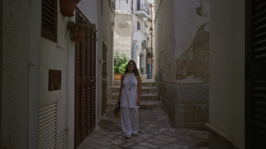 A young, hispanic woman explores the charming, narrow streets of polignano a mare, puglia, italy, dressed in stylish white attire and carrying a wicker basket.