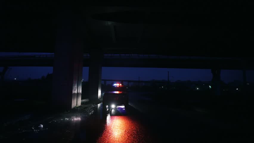 A dark urban roadway scene that showcases the vibrant emergency vehicle lights illuminating the area beneath a bridge