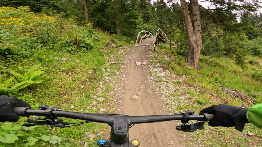 POV: Perspective of a mountain biker navigating down a winding and challenging wooden trail through a bike park. Fun, excitement and thrill of downhill adventures in beautiful mountain environment.