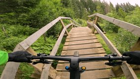 POV: Thrilling perspective of a mountain biker crossing a rustic wooden bridge while riding rugged trail in bike park. Sheer adrenaline during downhill biking in beautiful setting of mountain forest. - Powered by Shutterstock - Get 15% off with code: PIKWIZARD15