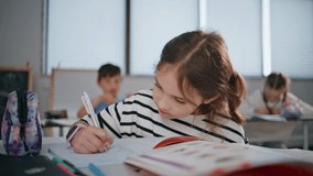 Clever schoolgirl studying classroom sitting at desk closeup. Thoughtful cute kid primary school student holding pen writing in exercise book. Smart pupil thinking answers learning at table indoors  - Powered by Shutterstock - Get 15% off with code: PIKWIZARD15