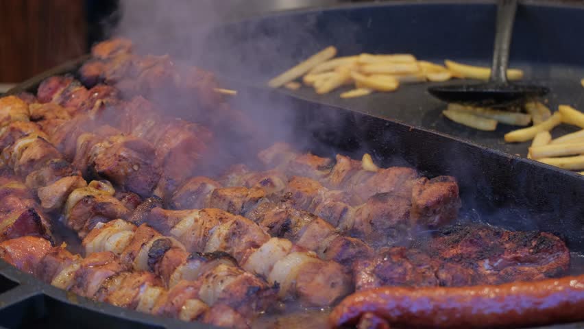 A close-up of a large grill on which a lot of meat and potatoes are being prepared.