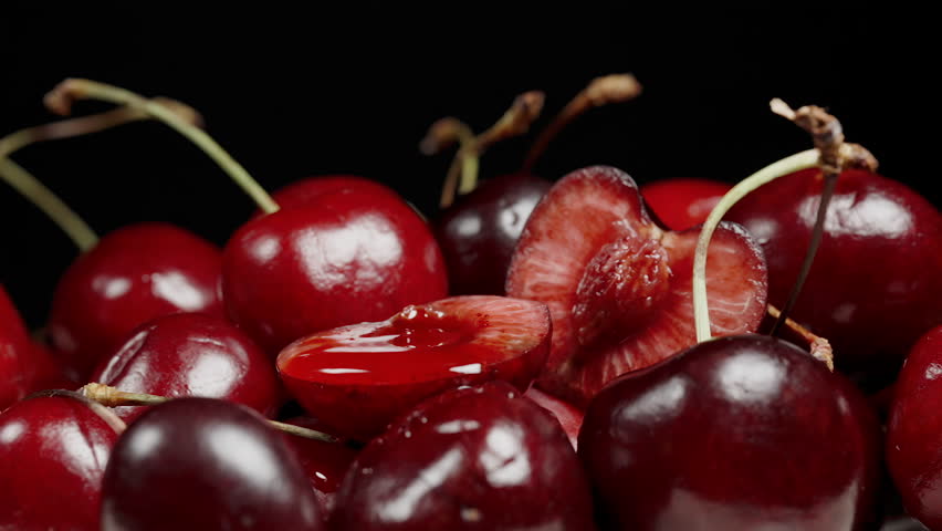 Hand Squeezing Juice from Cherry Half, Berries on Black Background, Macro. Slow Motion.