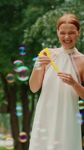 A woman joyfully blows bubbles while enjoying a sunny day in a vibrant park.