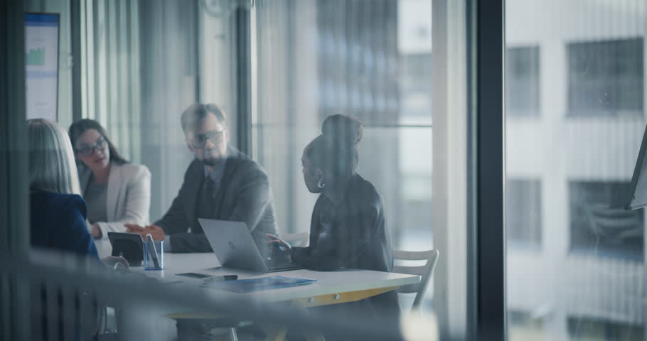 Diverse Team Engages in a Collaborative Strategic Planning Meeting in a Modern Glass-walled Conference Room. Office People Using Laptops and a Digital Whiteboard with Analytical Data