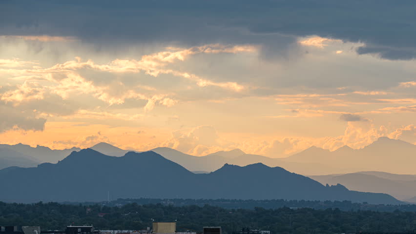 Sunset motion time lapse as golden clouds move over Rocky Mountain Range, Denver