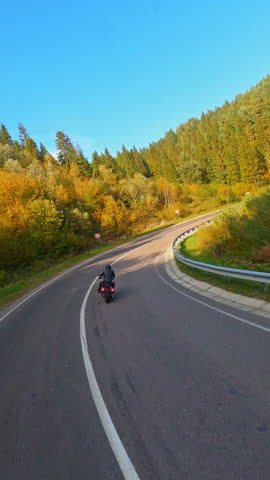 Aerial views of professional biker riding motorcycle along road in beautiful forest landscape. Motion FPV drone flight. Travel concept.
