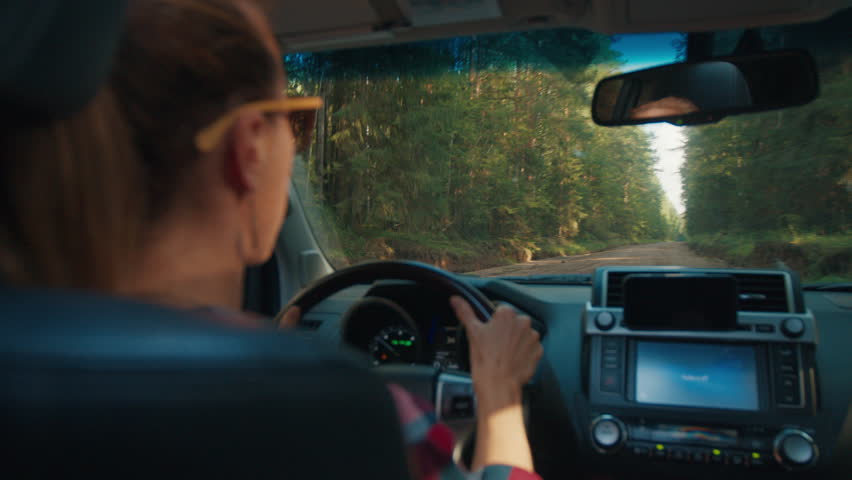 Woman steers the car on the summer unpaved bumpy road in the forest. Shaky handheld camera