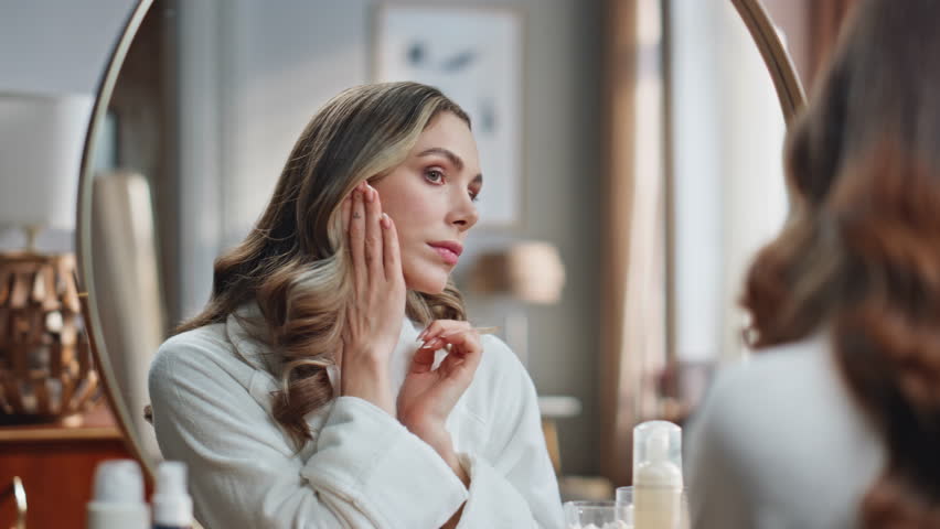 Involved woman lymphatic drainage procedures at mirror place. Closeup smiling lady touching face making facial self massage at home. Calm model doing domestic skin care treatment at light bathroom 