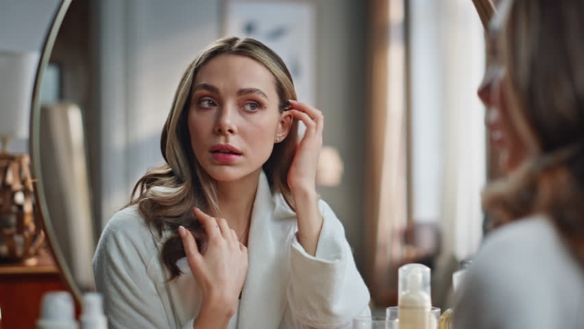 Beautiful lady touching skin looking mirror indoors closeup. Young woman doing face lifting self massage at bathroom. Focused model making mimic gymnastics exercises. Beauty care at house concept