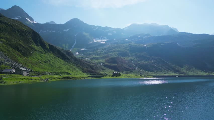 A stunning drone view over the Splügen Pass, capturing crystal-clear alpine lakes surrounded by towering mountains. The serene landscape showcases nature