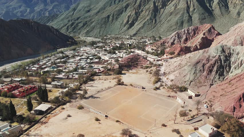 Drone aerial views nature scenes, a mountain city setting, football field place near the residential area between the mountains surrounded by scarce amount of vegatation, zoom in 