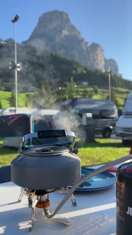 an outdoor water kettle steaming in a campsite with stunning mountain peak in the background, Dolomites, Italy