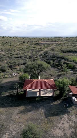 Cottage. Construction in the middle of a rural landscape. Panoramic aerial view with drone. Vertical video. Cloudy sky in the background. 