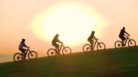AERIAL, SILHOUETTE, LENS FLARE: Stunning sunset with group of mountain bikers riding up the grassy hill. Picturesque bike ride through the green, hilly Slovenian countryside in beautiful golden light. - Powered by Shutterstock - Get 15% off with code: PIKWIZARD15
