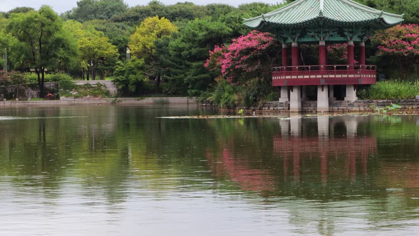A drizzle is falling on the pond, and an octagonal pavilion surrounded by Crape Myrtle trees is visible.