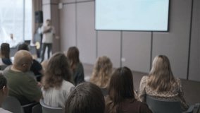 Group of people attentively listens to a presentation in a modern conference room. The speaker is presenting at the front with a large screen displaying visuals. - Powered by Shutterstock - Get 15% off with code: PIKWIZARD15