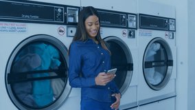 Digital communication icons animation over woman using smartphone in laundromat. Technology, social media, connectivity, multitasking - Powered by Shutterstock - Get 15% off with code: PIKWIZARD15