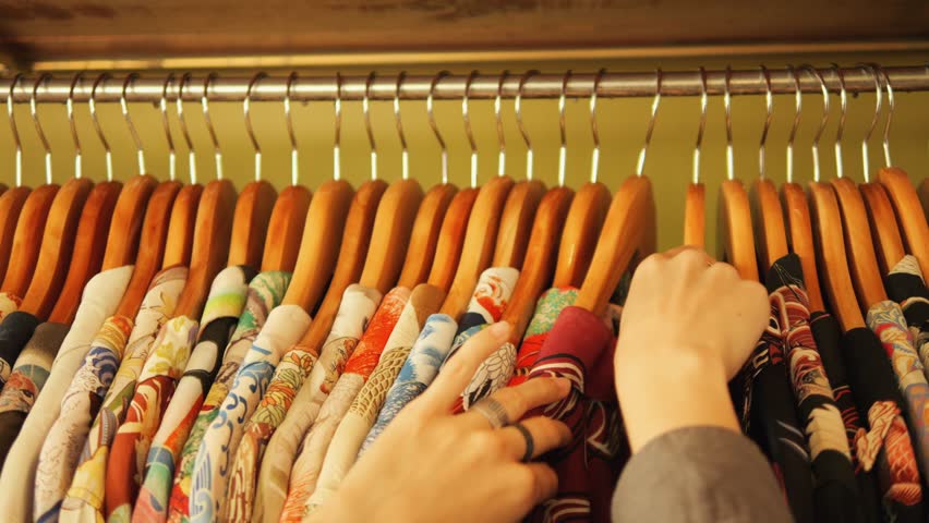 Elegant Female Hands Sorting Through Hangers With Bright National Printed Shirts On A Clothing Rack In A Vintage Clothing Store