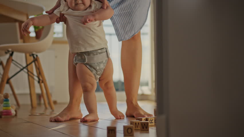 A child's first steps are a touching moment of growing up. A caring mother carefully holds her child by the hands. She patiently teaches the baby to walk. Early childhood education