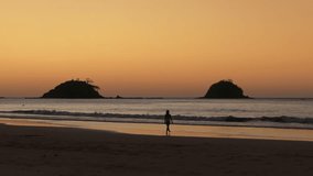 Aerial view of a silhouette woman walking on a tropical beach island with beautiful orange sunset sky. Travel video of woman relaxing in vacation in Nacpan beach Philippines  - Powered by Shutterstock - Get 15% off with code: PIKWIZARD15